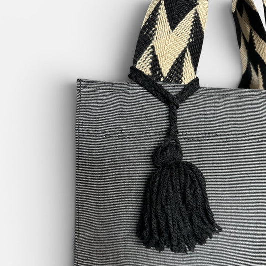 Gray tote bag with a decorative strap and tassel on a light gray background
