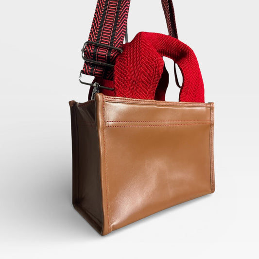 Brown leather bag with a red knitted item inside on a light gray background