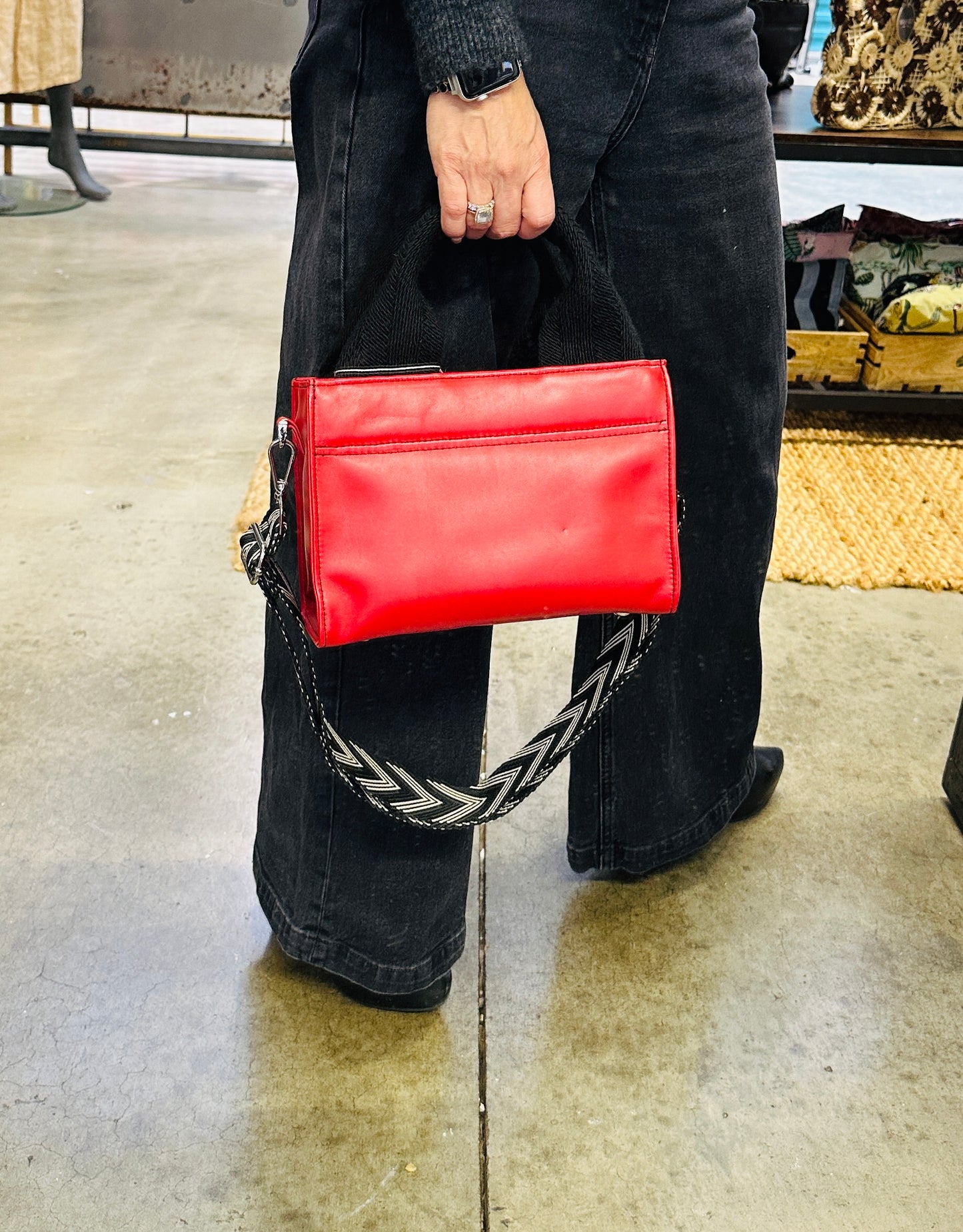 Person holding a red handbag with a chain strap on a concrete floor.