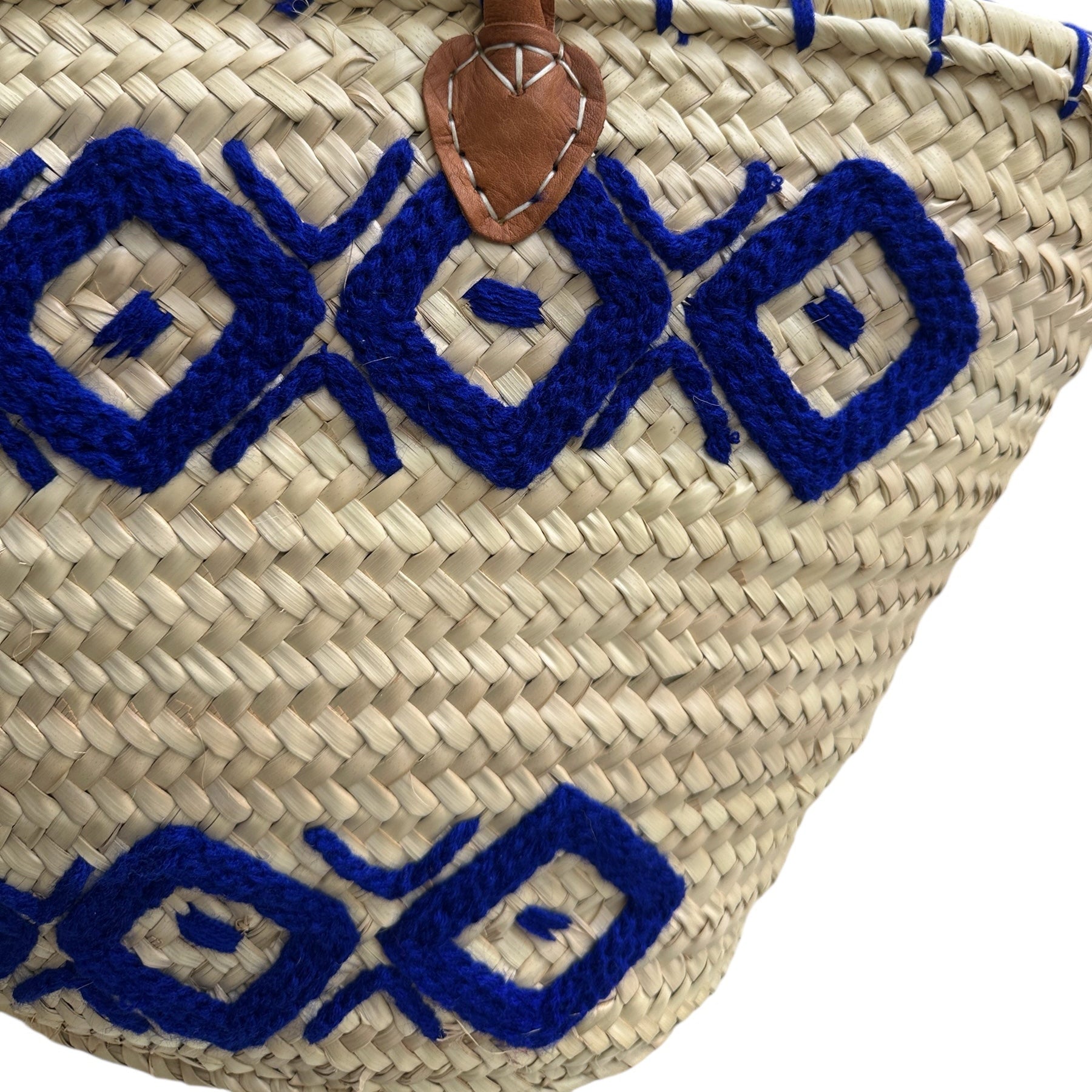 Woven bag with blue geometric patterns and brown handles on a white background