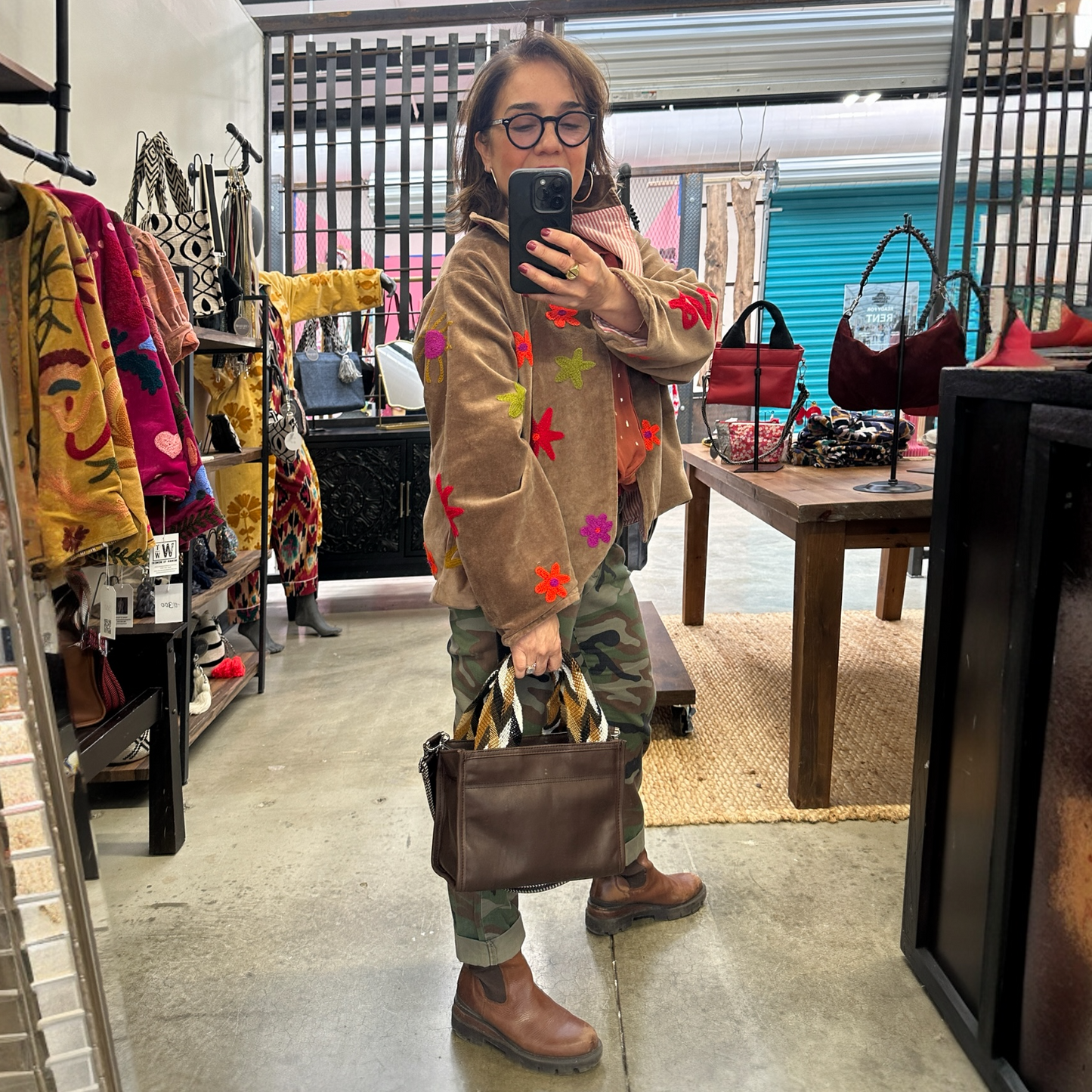 Person taking a mirror selfie in a store holding a brown handbag.