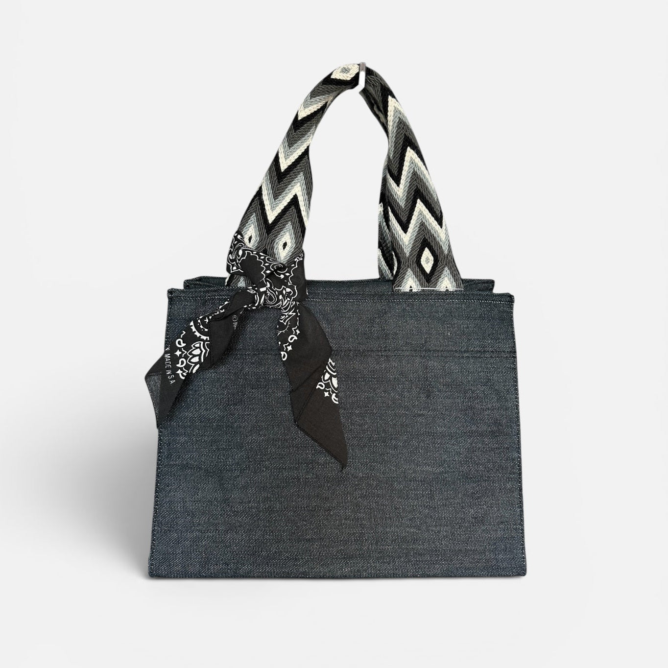Dark gray tote bag with a black and white zigzag patterned handle on a light gray background