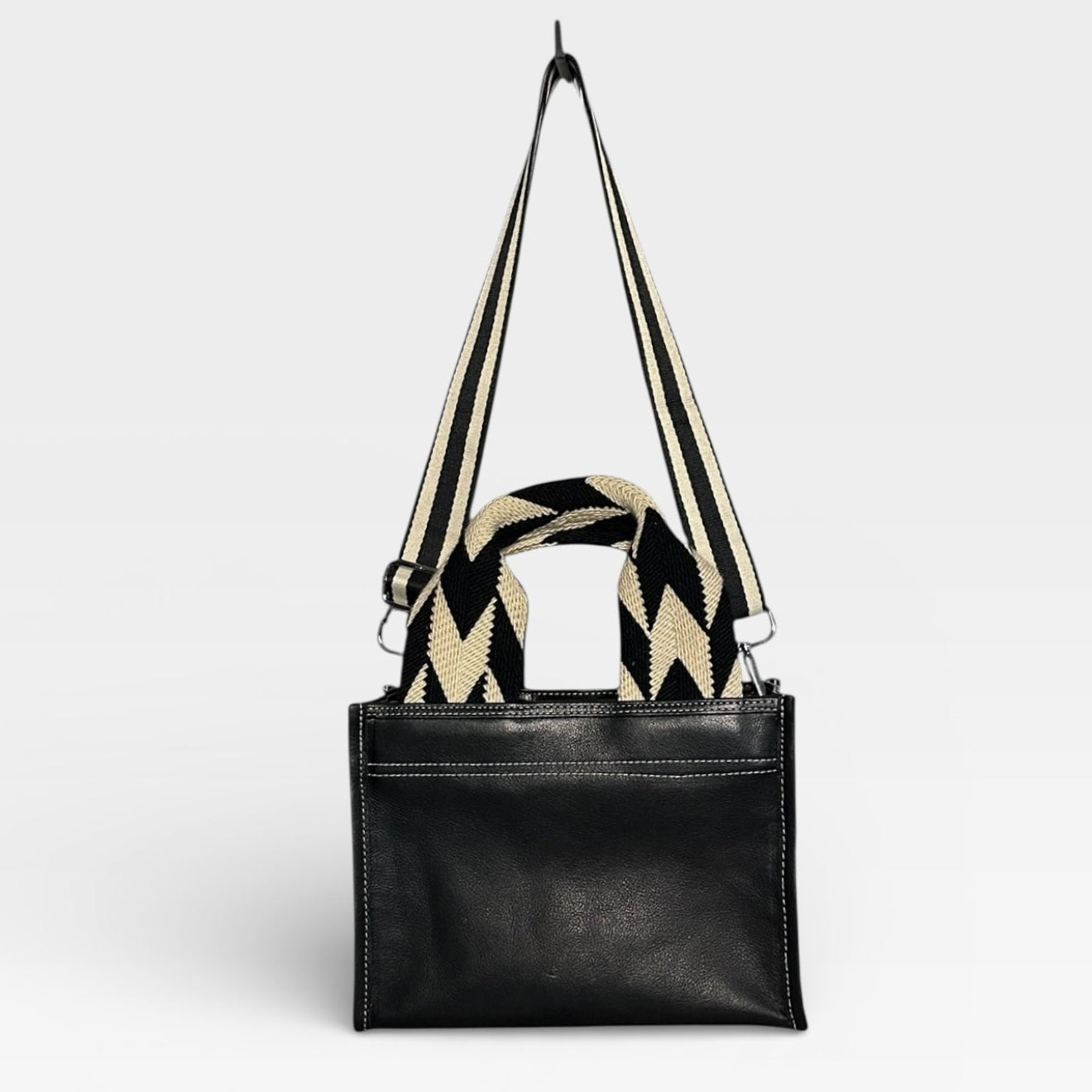 Black handbag with a patterned strap on a light gray background
