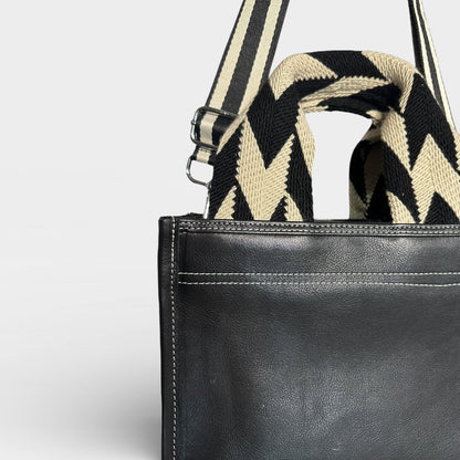 Black leather bag with a striped shoulder strap on a light gray background