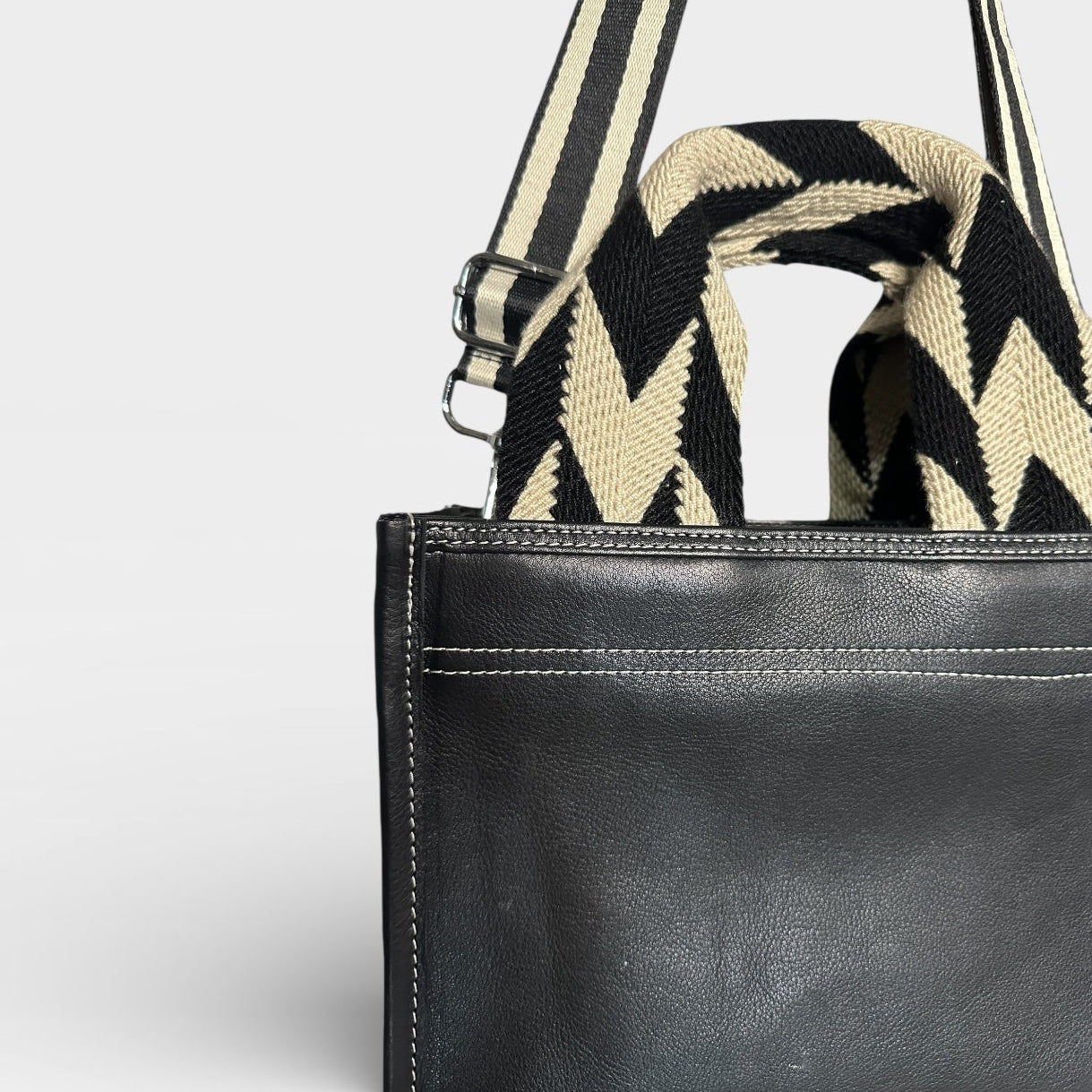 Black leather bag with a striped shoulder strap on a light gray background