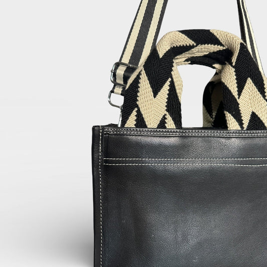 Black leather bag with a striped shoulder strap on a light gray background