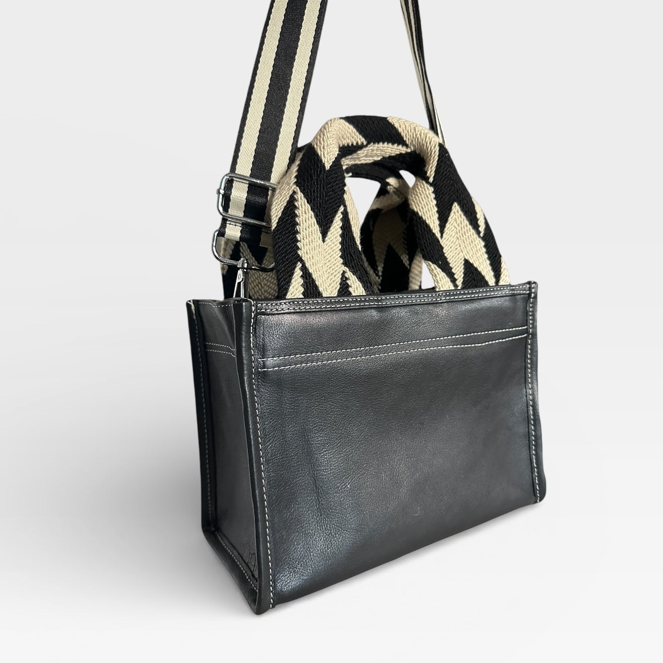 Black leather handbag with a striped strap on a light gray background