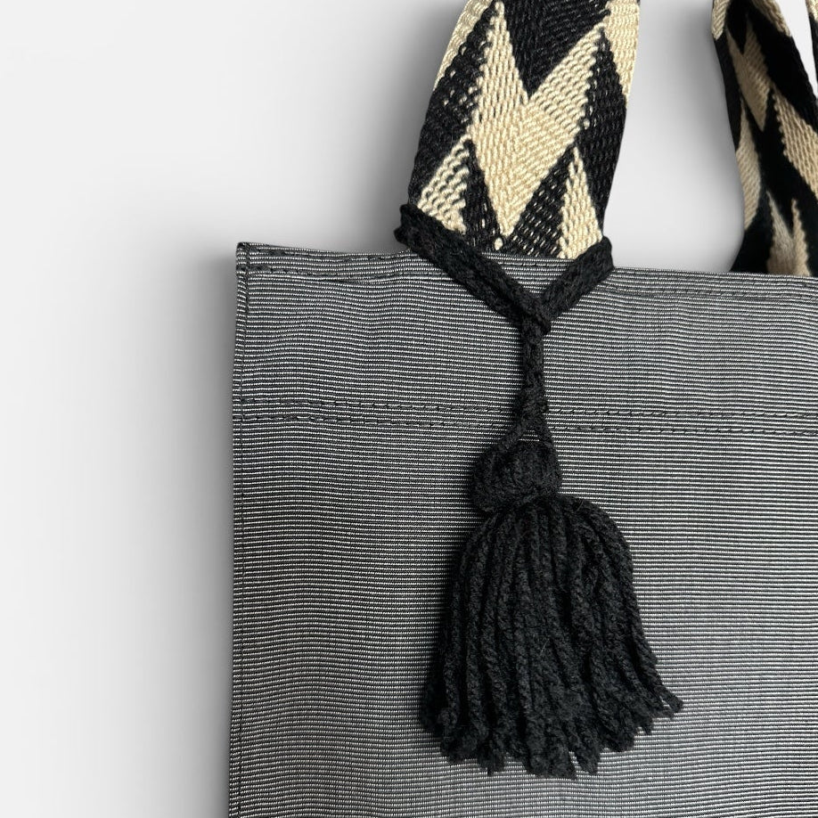 Gray tote bag with a decorative strap and tassel on a light gray background