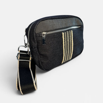Black crossbody bag with gold zipper details on a light gray background