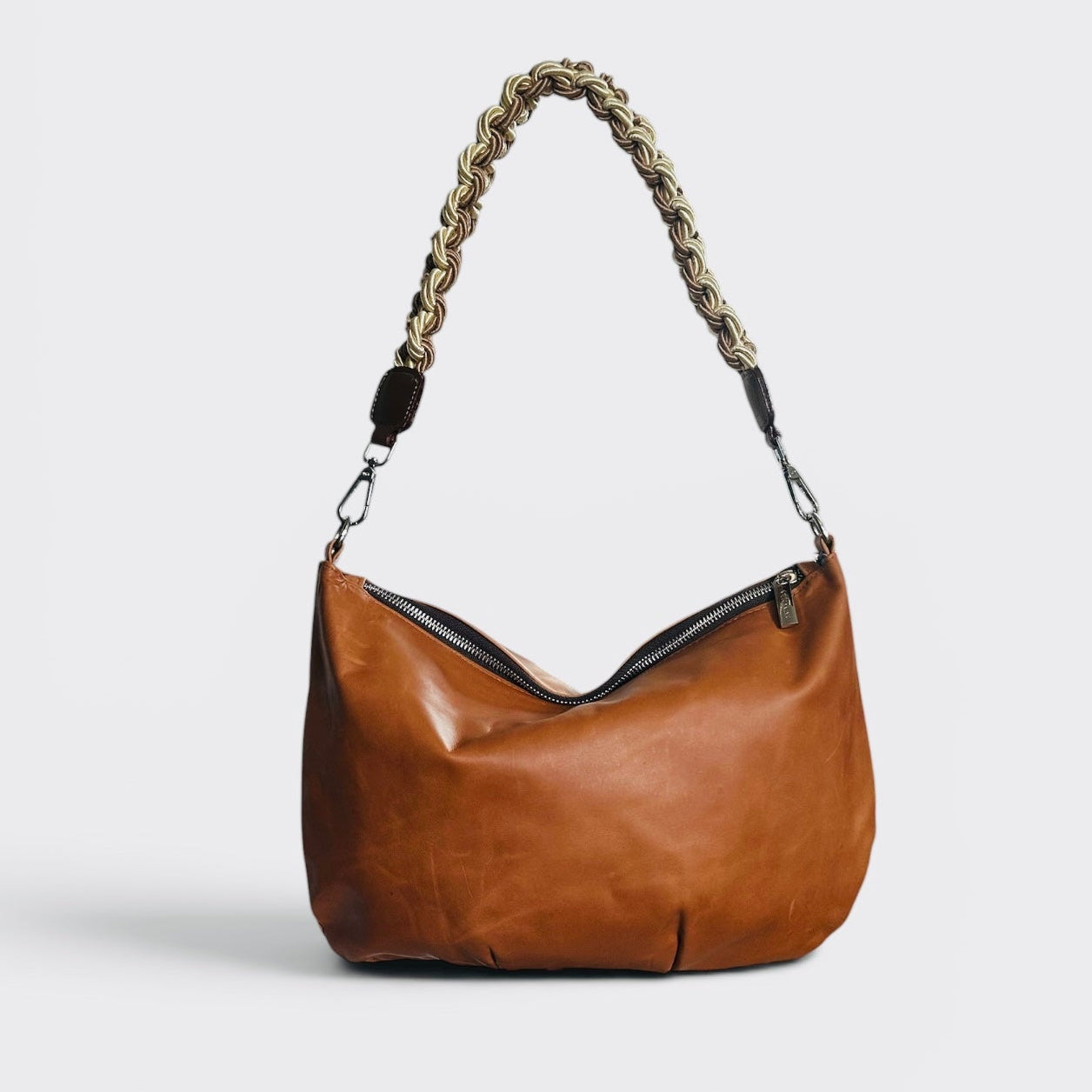 Brown leather handbag with braided handle on a light gray background