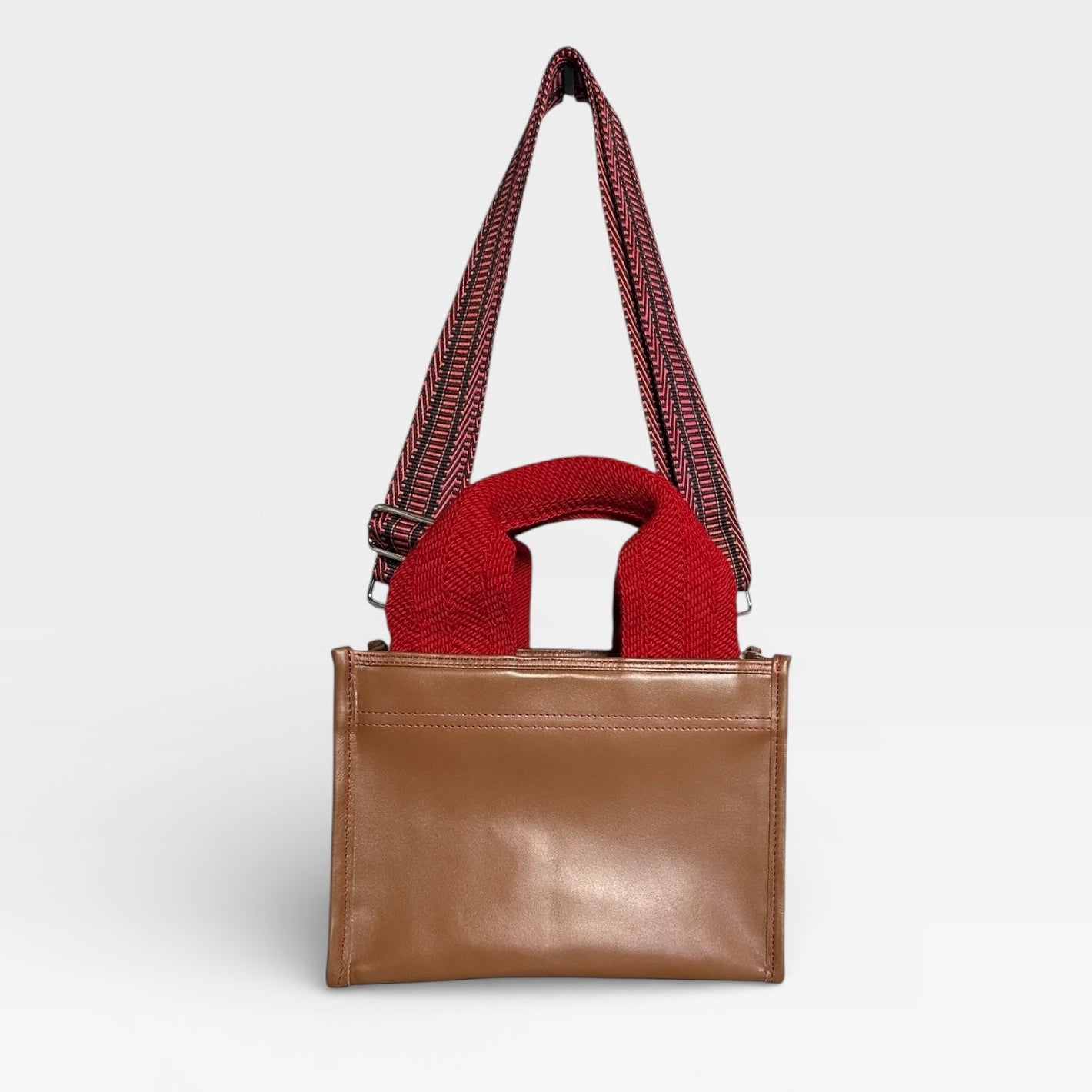Brown handbag with a red interior and strap on a light gray background