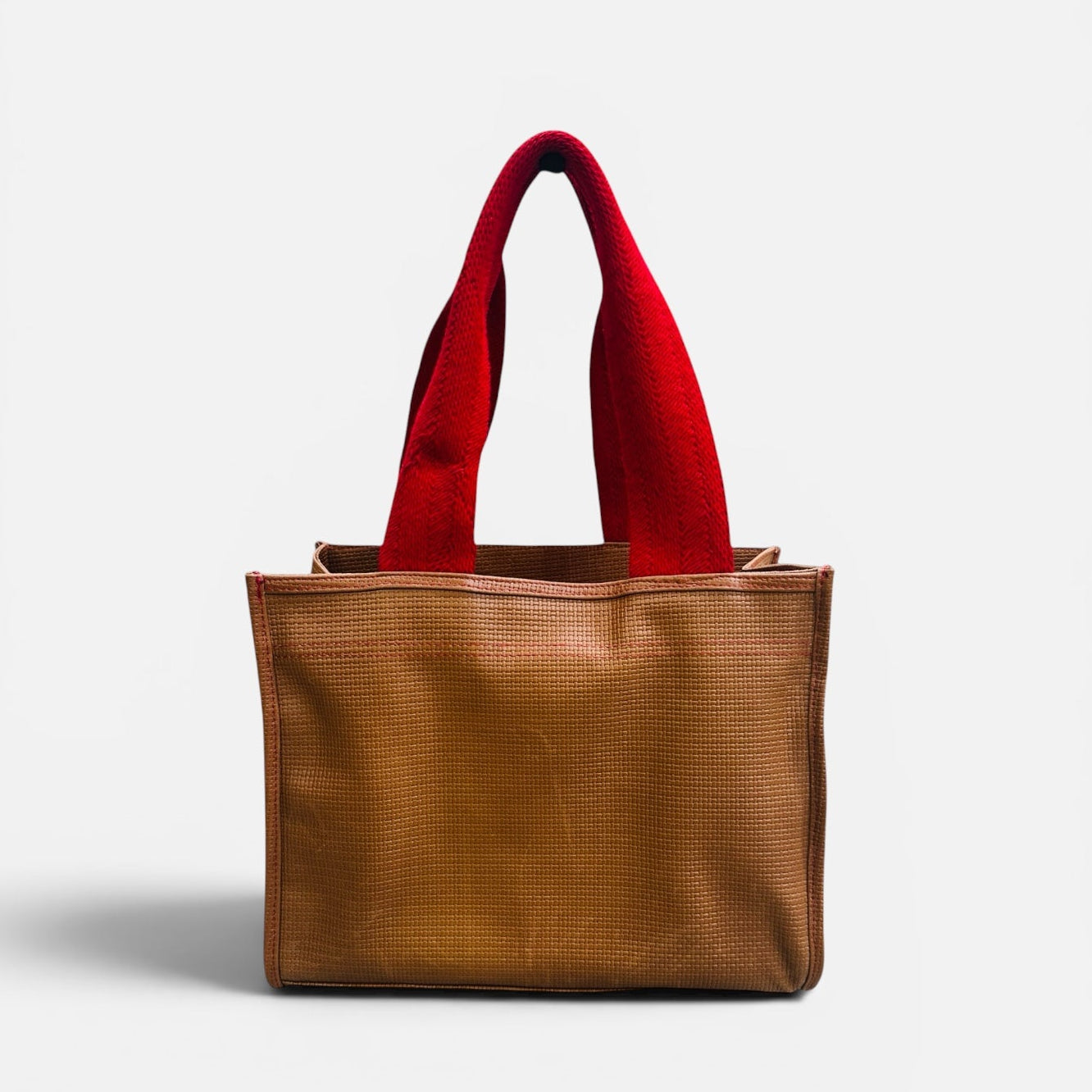 Brown tote bag with red handles on a light gray background