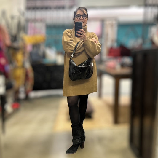 Person taking a mirror selfie in a store aisle wearing a beige coat and black shoes.