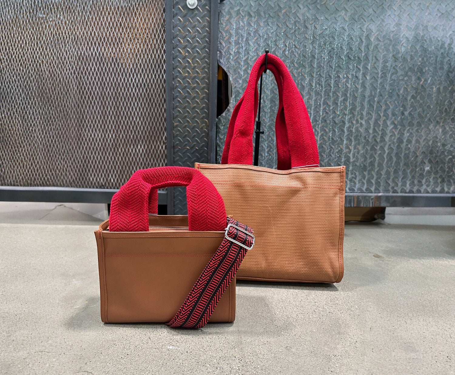 Two handbags, one brown and one red, with a strap on a textured surface.