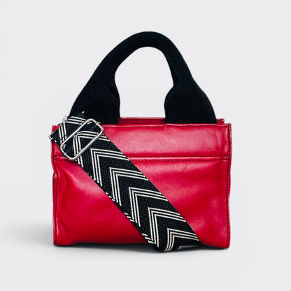 Red handbag with a black and white zigzag strap on a light gray background