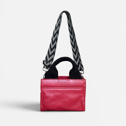 Red leather handbag with a black and white zigzag strap on a light gray background
