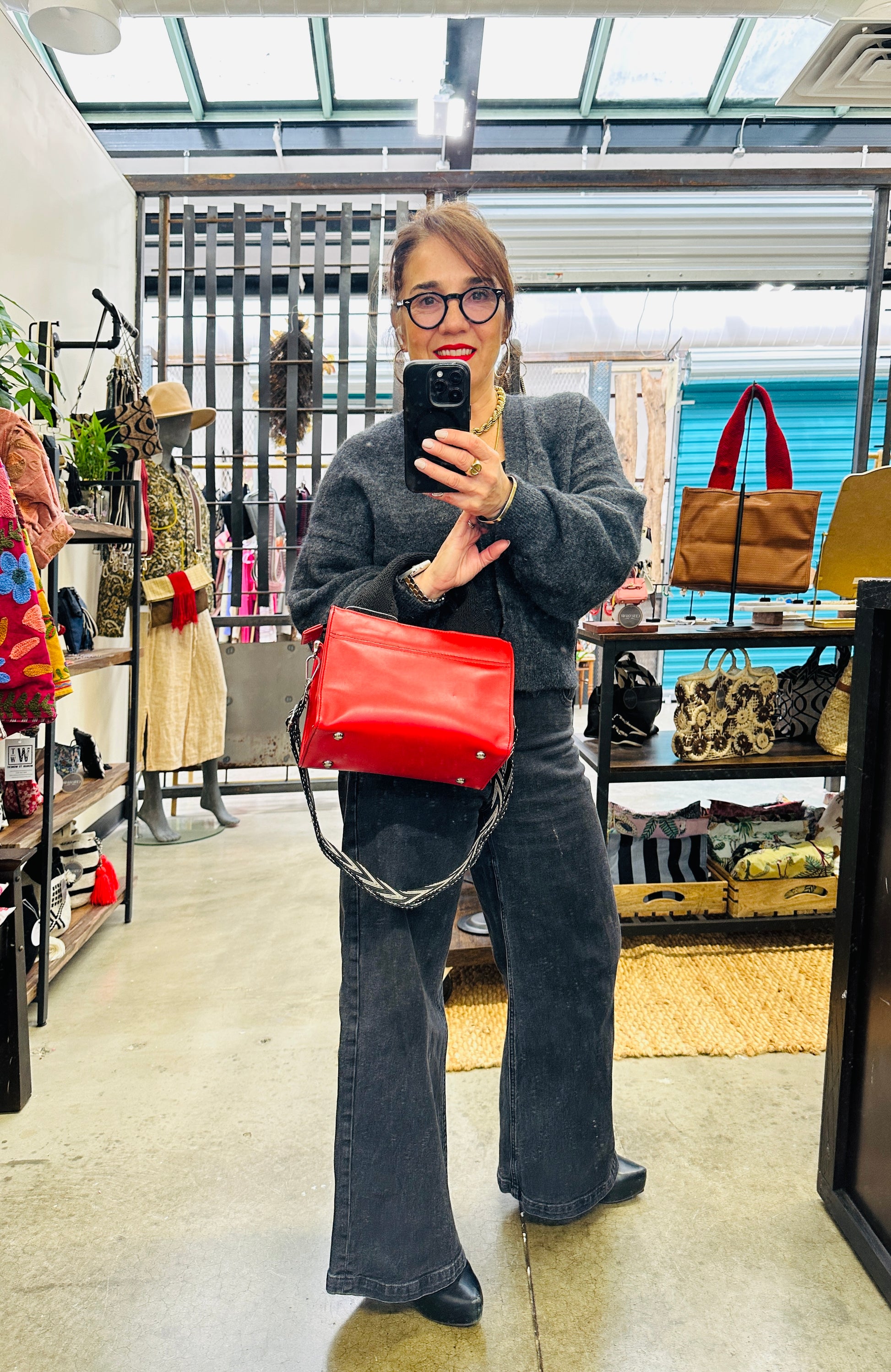 Person taking a mirror selfie in a store holding a red handbag.