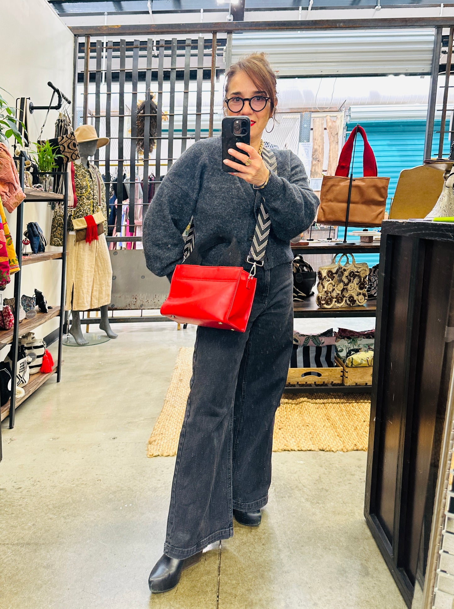 Person taking a mirror selfie in a store with a red handbag
