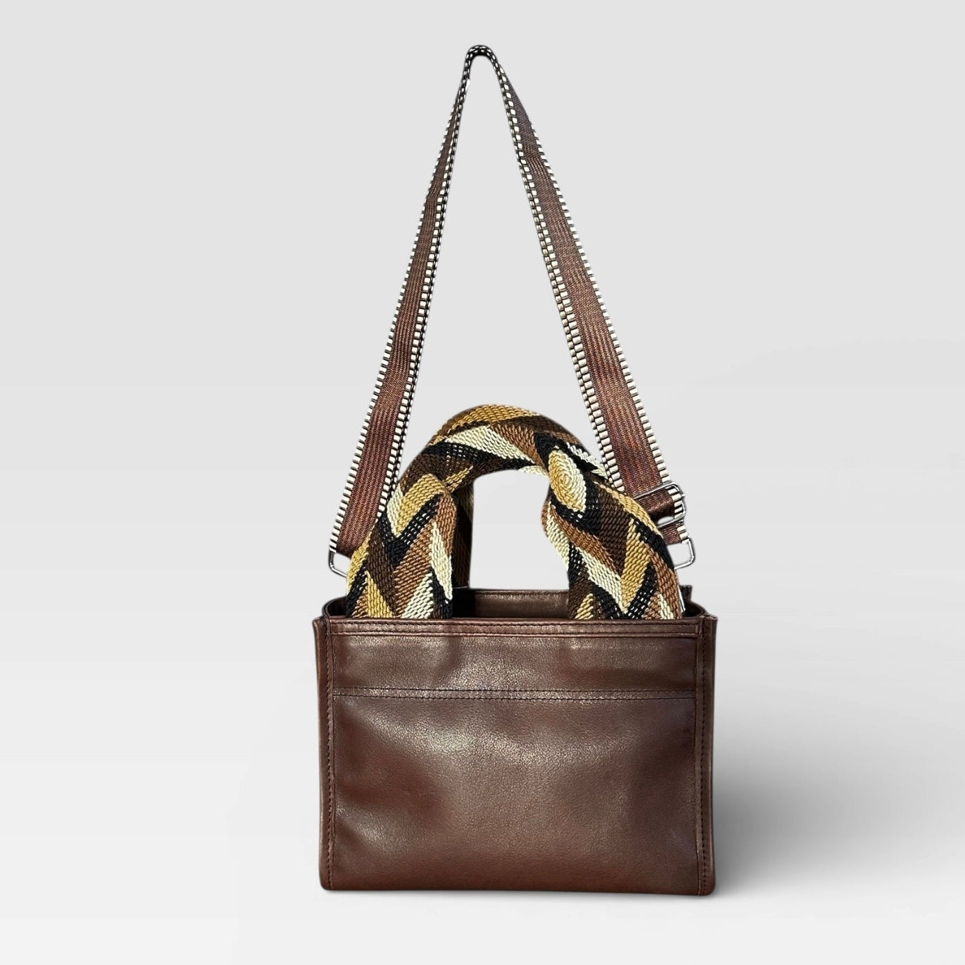 Brown leather handbag with a zigzag strap on a light gray background