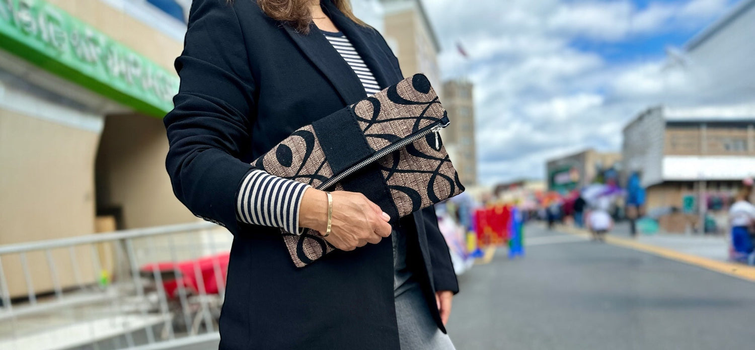 Person holding a patterned clutch on a crosswalk with a store and people in the background
