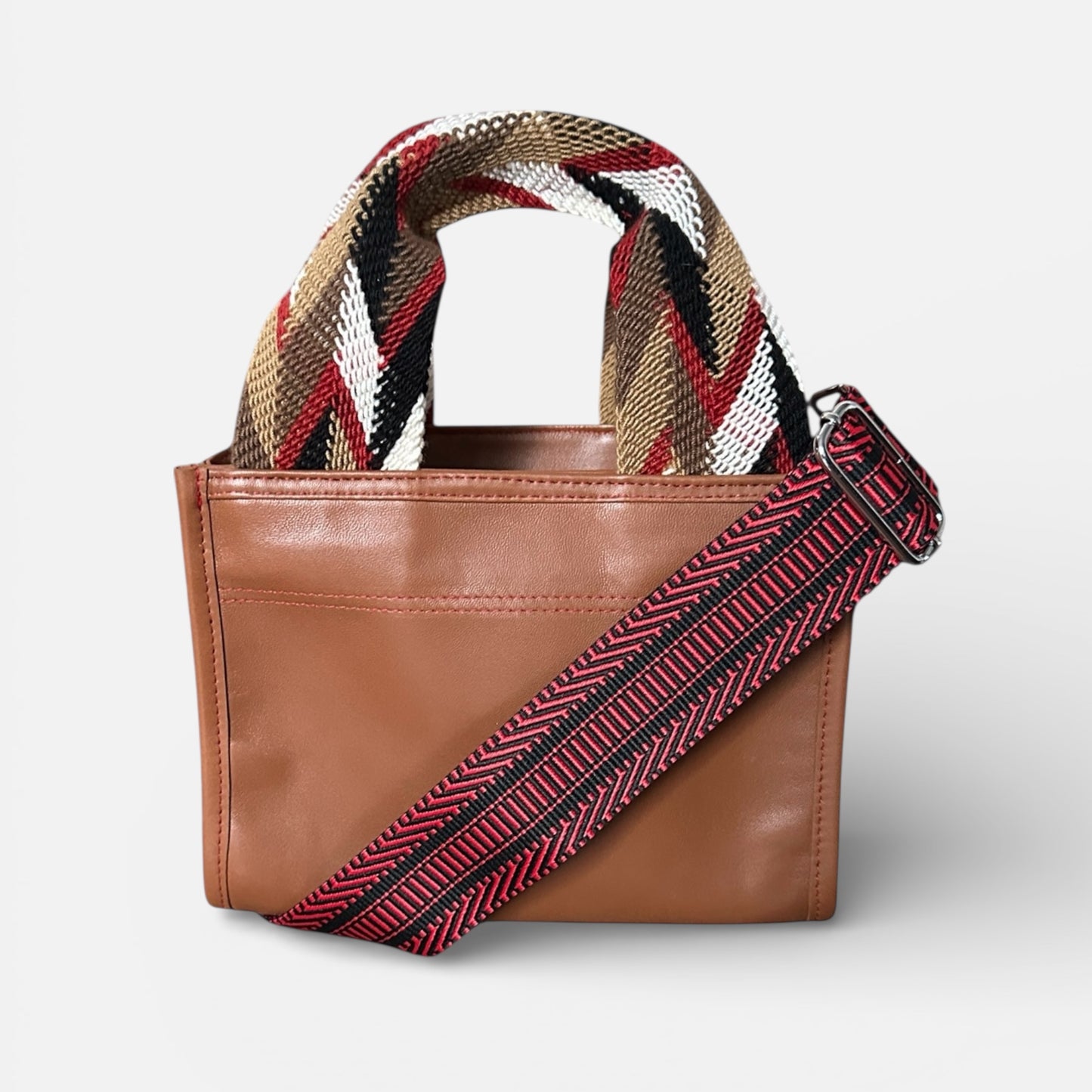 Brown leather handbag with a colorful woven strap on a light gray background