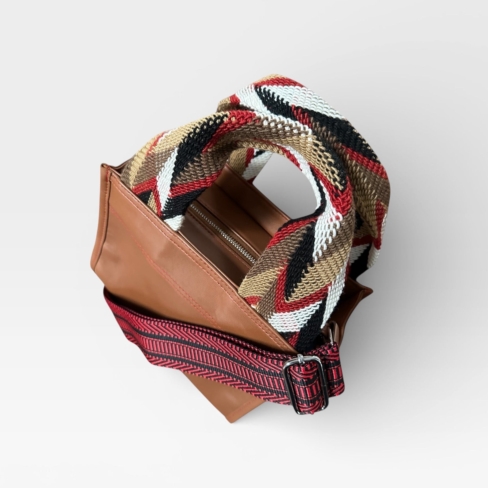 Brown leather clutch with a colorful woven strap on a white background