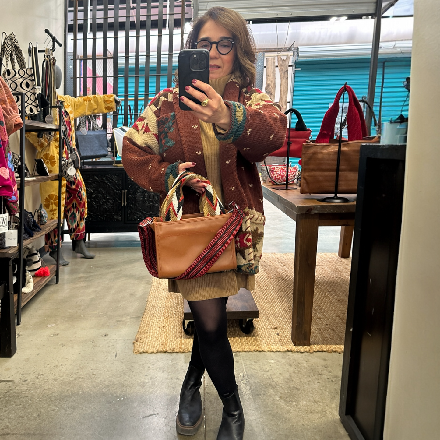 Person taking a mirror selfie in a store holding a brown handbag.