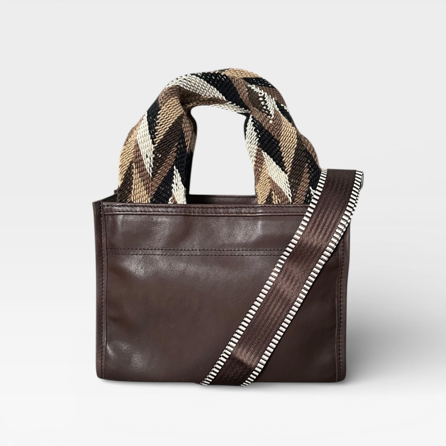 Brown leather handbag with patterned handle on a light gray background