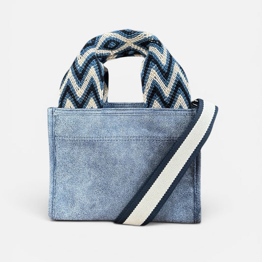Blue denim handbag with a zigzag patterned handle on a white background