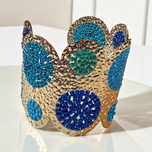 Cuff bracelet with blue and green circular patterns on a white surface.